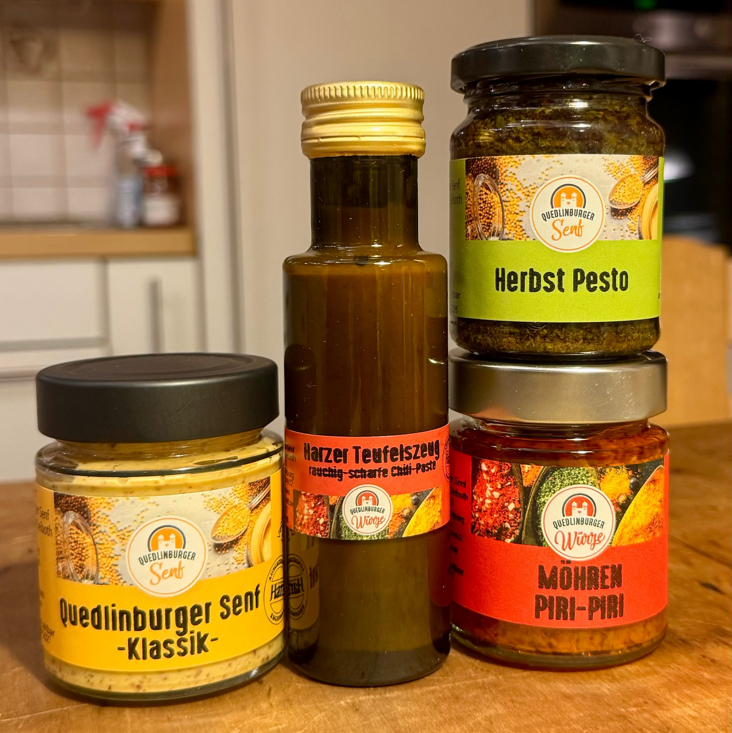 Vier große Gläser (Klassik-Senf, Möhren-Piri-Piri, Kräuterpesto, Teufelszeug) als veganes Probier-Set, arrangiert in natürlicher Küchen- oder Holzoptik – mild bis scharf.