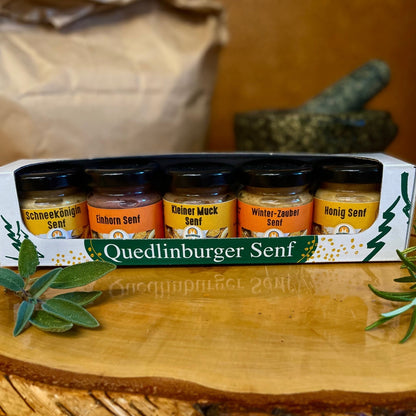 Fünf kleine Senfgläser im Märchen-Set, dekorativ arrangiert auf Holztisch mit herbstlicher Deko. 5 Mini-Senfe aus der Quedlinburger Senf-Manufaktur – süß, fruchtig &amp; würzig.